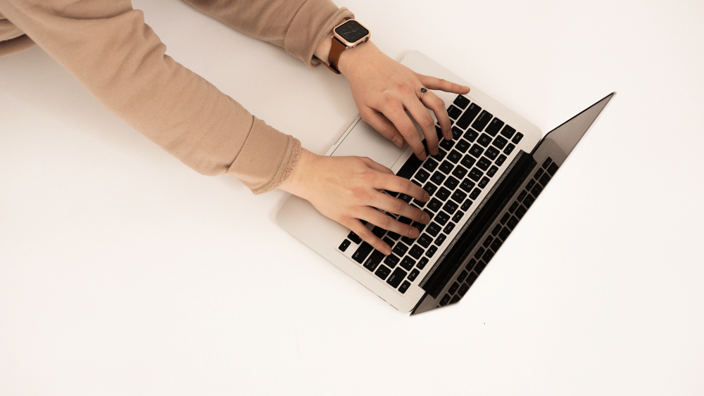 Person sitting at white desk typing on laptop searching for a generative engine optimization agency - Dig & Dig