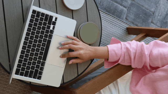 Person in pink top sitting at a table outside with coffee on laptop looking at generative engine optimization - Dig & Dig