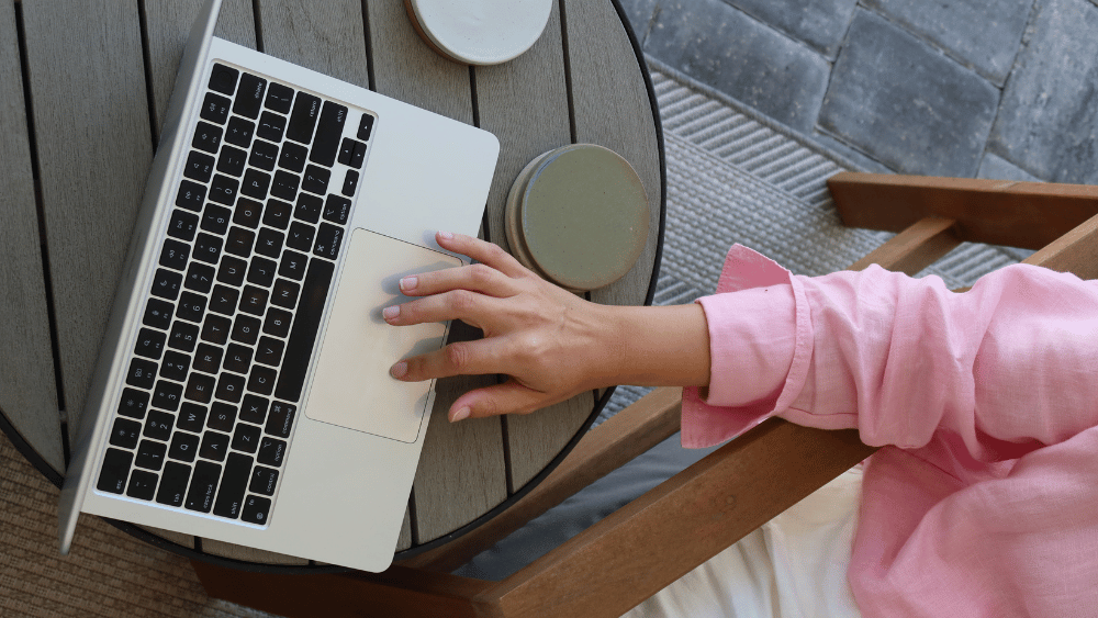Person in pink top sitting at a table outside with coffee on laptop looking at generative engine optimization - Dig & Dig