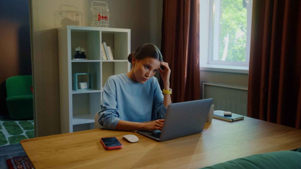 Young adult sitting at desk looking stressed at laptop - Dig & Dig
