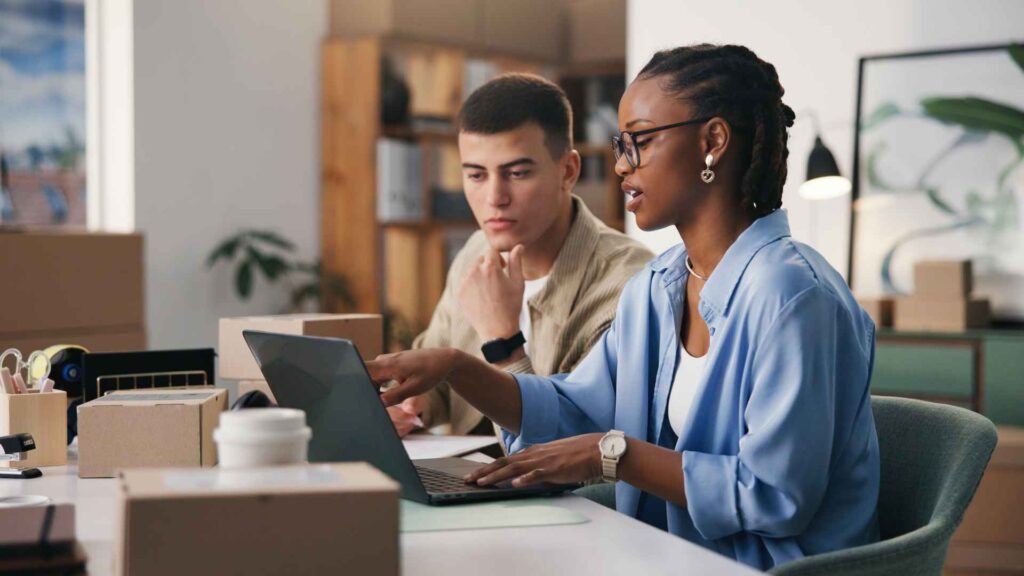 Two young people sitting at desk looking at laptop - Dig & Dig